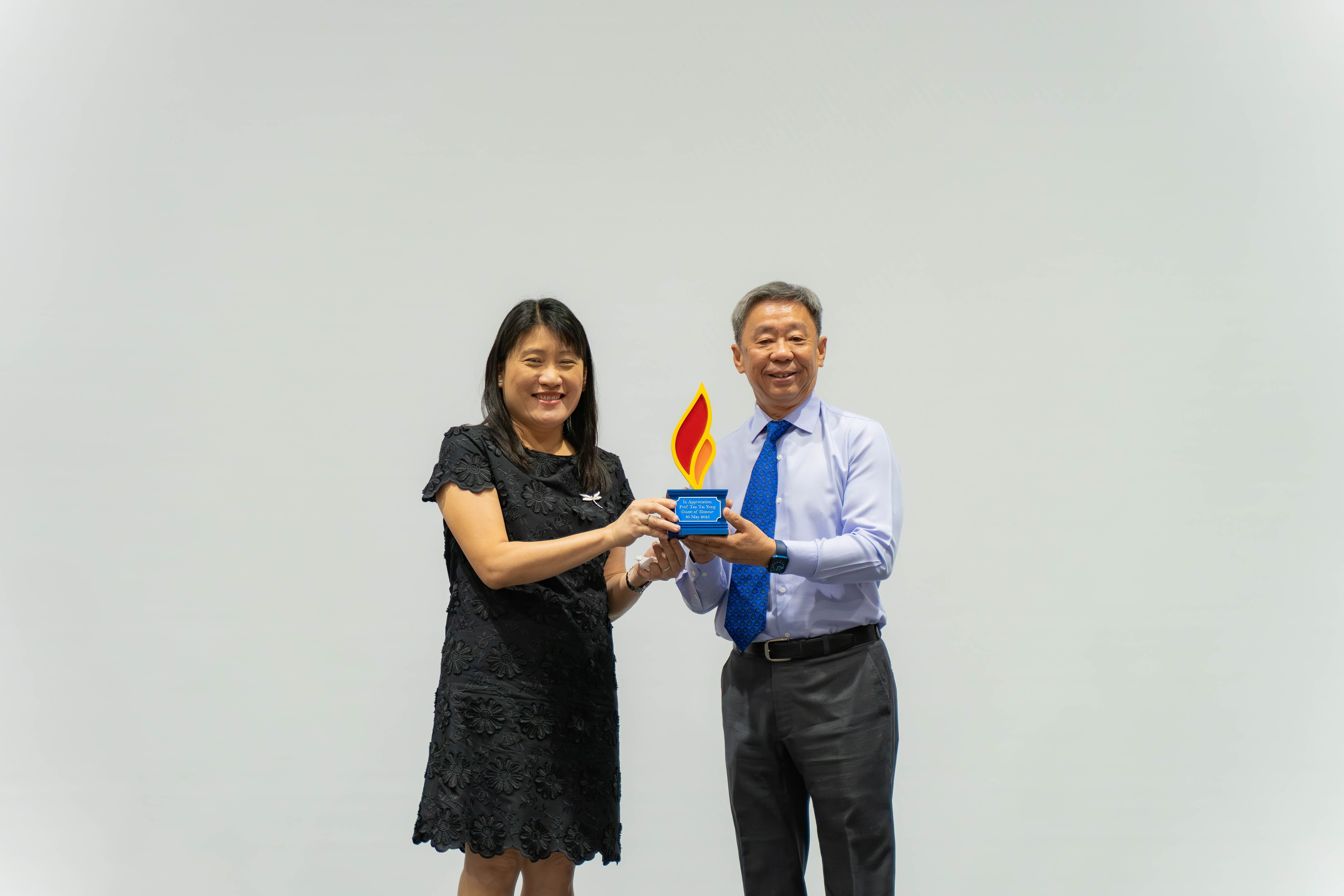 Two people smiling and holding a blue award trophy with red and yellow flame shapes together.